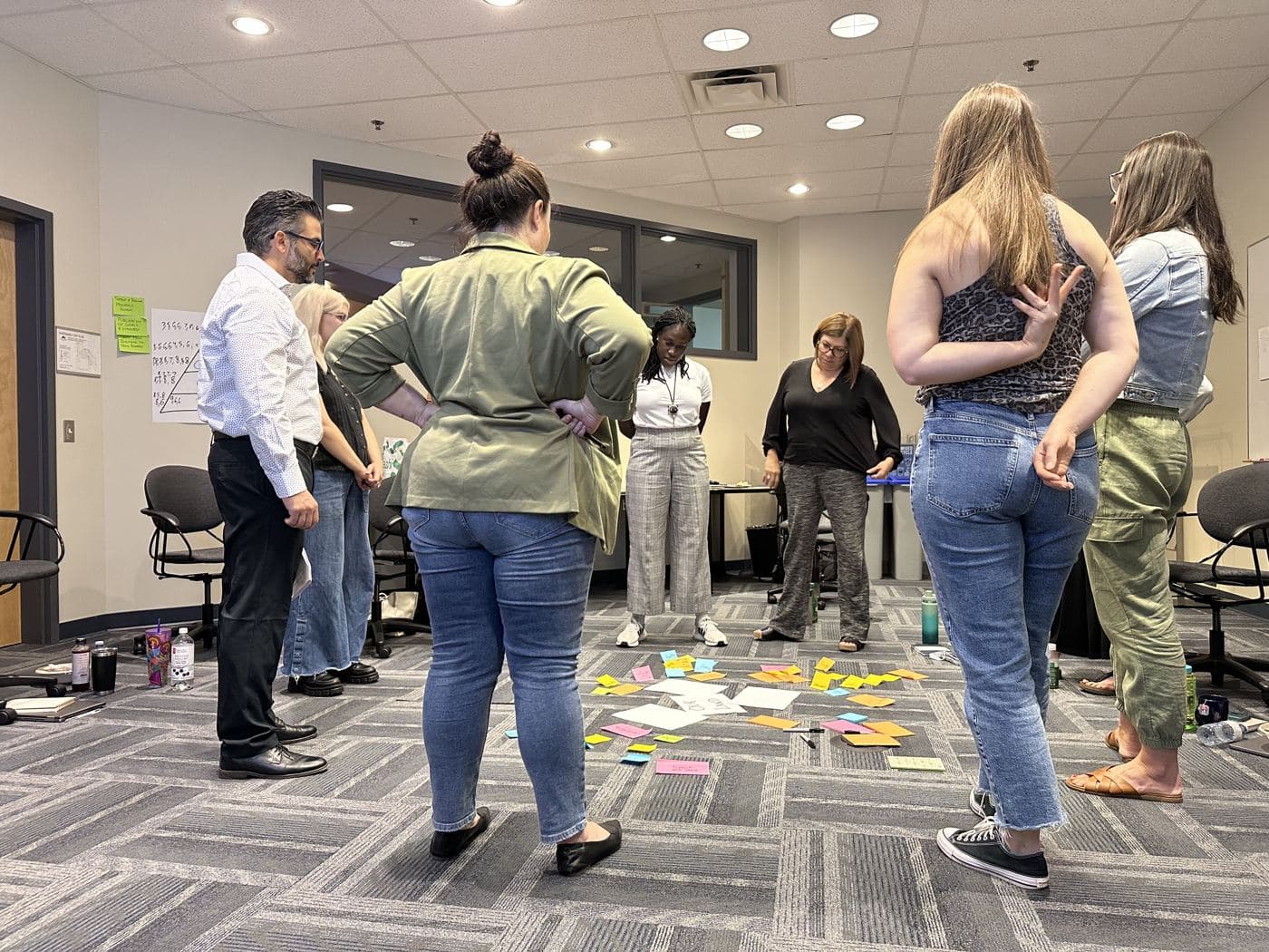 A team stands in a circle around lands taped on the floor, scattered with sticky notes