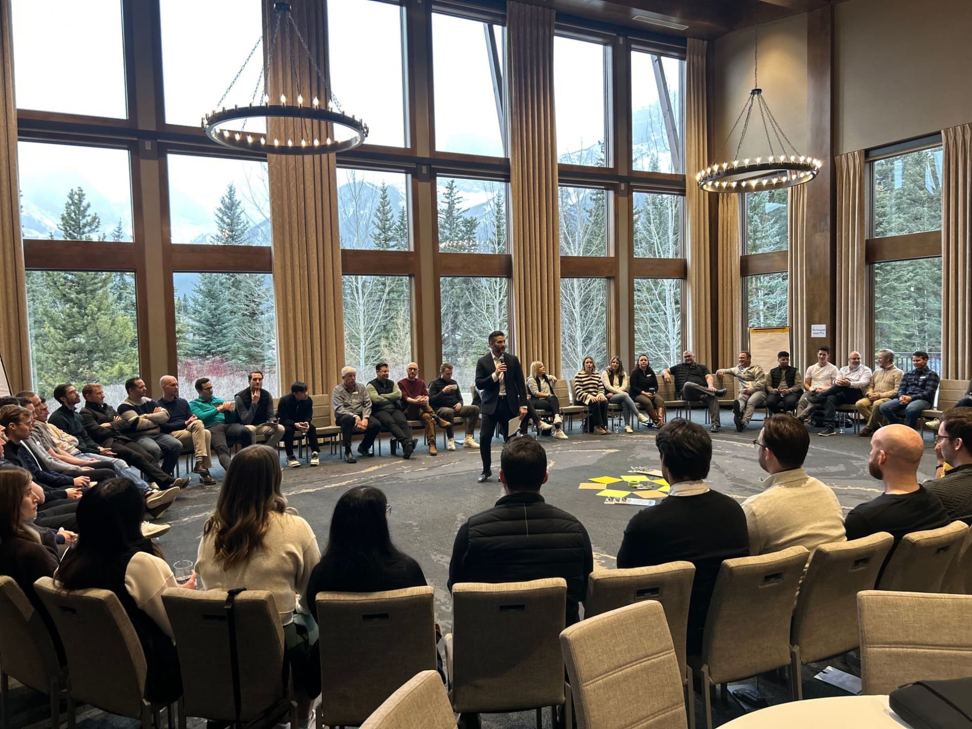 A facilitator leading a large group seated in a circle in a mountain-view meeting room