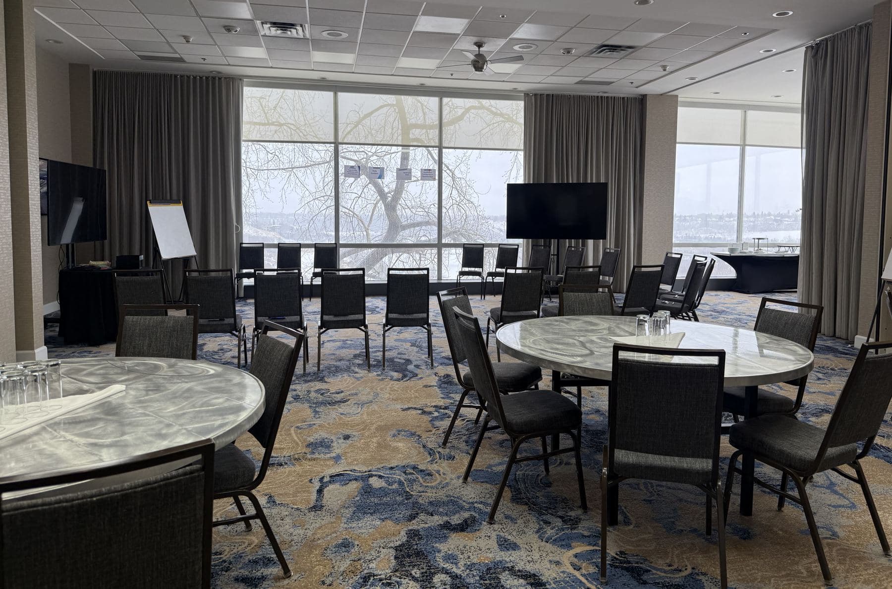 A workshop room set café style with round tables and chairs in front of tall windows